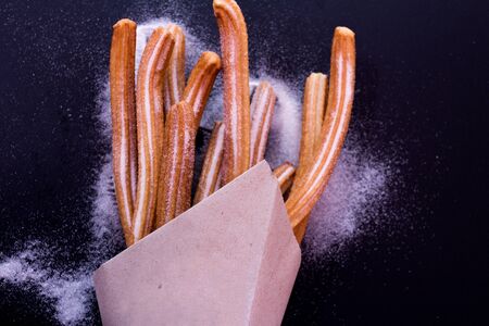 Churros sticks fresh hot with sugar in paper bag on dark background