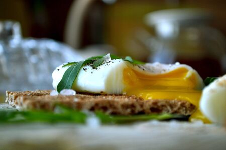Poached egg on a whole grain bread with arugula on a wooden table. Tasty and healthy breakfast.の写真素材