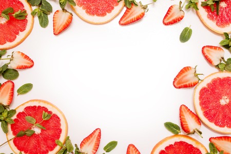 Cute flat lay with fresh fruit, sliced strawberry and grapefruit or red orange, mint leaves on white background. Fresh and juicy frame with free space in the centerの写真素材