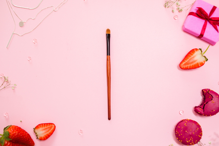 Cute pink flat lay, with a fine makeup brush in the center . Glamorous style, elements cosmetics and sweets on frameの写真素材