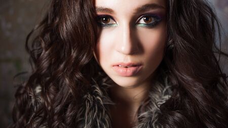 Attractive young brunette woman in stylish fur collar made of eco fur. Portrait in a dark mysterious styleの写真素材