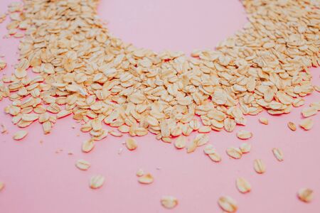 healthy diet, the concept. Grain oatmeal on a pink background. Oat flakes scattered, copy space