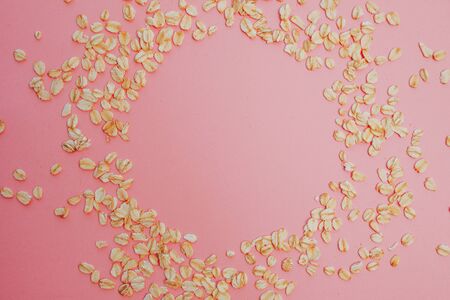 Oatmeal grains on pink background, copy space. Oat flakes lie in the form of circle, free place for...
