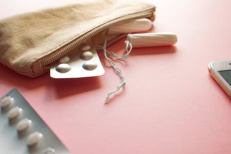 Cosmetic bag or handbag with tampons, contraceptives and pain pills. Set in case of menstruation. Pink backgroundの写真素材