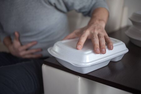 Food delivery from the restaurant. Problems of poor quality products and food allergies. Food poisoning, stomach trouble. A man holding a sick stomach, food containers in the foregroundの写真素材