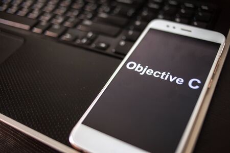 Objective C Programming language for mobile development, concept. Smartphone on the laptop keyboard, the programmer's workplaceの写真素材