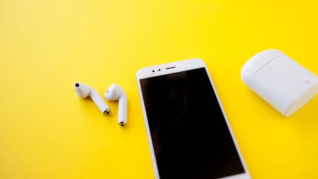 White wireless headphones and smartphone are lying on a bright background. Headphones out of...