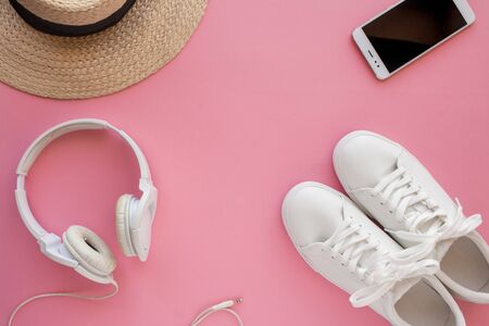 White sneakers, straw hat, headphones, smartphone and are lying on a bright pink background. Top...