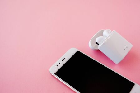 Wireless headphones and smartphone are lying on a bright pink background. Headphones in charging case. Top view. Copy space top left.の写真素材