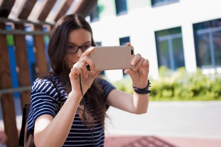 A pretty young woman, a student, a brunette with glasses, youth clothes and a backpack sits on a...