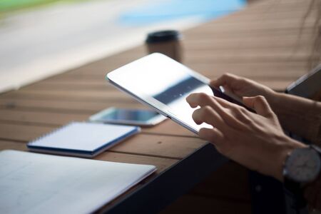 Women's hands with neat low-key manicure and with large wristwatch, work with gadgets, tablet,...