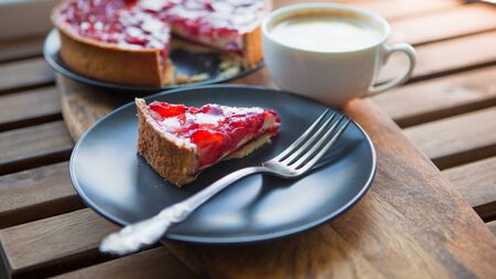 Still life with a Cup of coffee and sweet dessert with strawberries, cheesecake cake with slices of berries in jelly on top. Breakfast at home or on the veranda, a piece of cheesecake with cappuccino.の写真素材