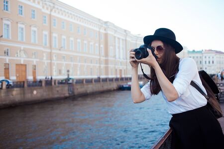 Funny hipster girl taking pictures in the city. A young woman with a hat and a camera. Tourist takes a photo of the cityの写真素材
