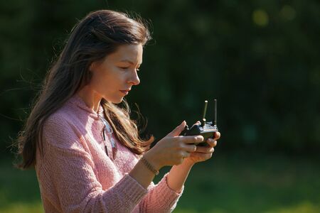 A woman in a clearing in the park watches a drone flying through the control panel monitor, which...