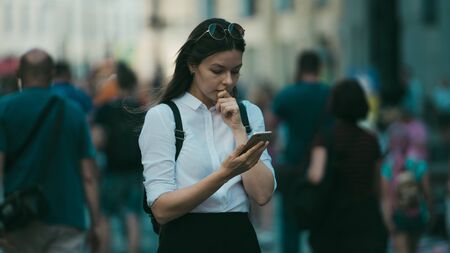 Girl on the street among the crowd of passers-by, photos in the style of surveillance. young woman in the city uses her phone to find a route, uses the Internet and mobile applications.の写真素材