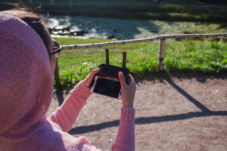 A young woman in a pink hoodie and sunglasses sitting on a stone bench and operated by remote...