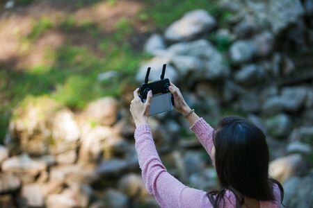 Everything's under control. A young woman in a forest with a drone control panel looks out for...