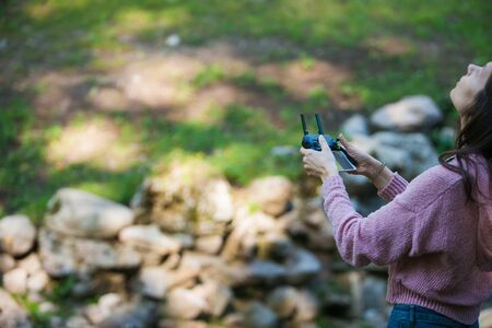 Everything's under control. A young woman in a forest with a drone control panel looks out for...
