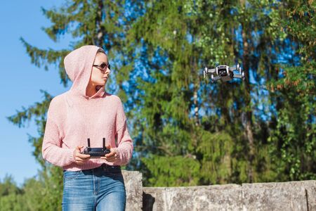A young woman in a pink hoodie and dark glasses holds, launches, catches the drone with one hand,...