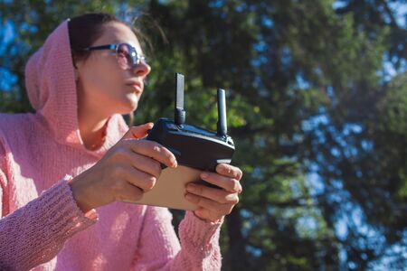 A young woman in a pink hoodie and sunglasses sitting on a stone bench and operated by remote...