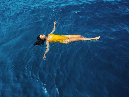 young woman in a one-piece yellow swimsuit floats on the surface of the water. Brunette girl relaxes...