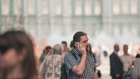guy in a crowd on a big city street. A young bearded man in the city uses a mobile phone, talking on the phone, a business conversation.の写真素材
