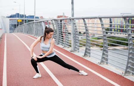 City fitness. A young sports woman in a fitness suit is warming up, doing stretching against the...