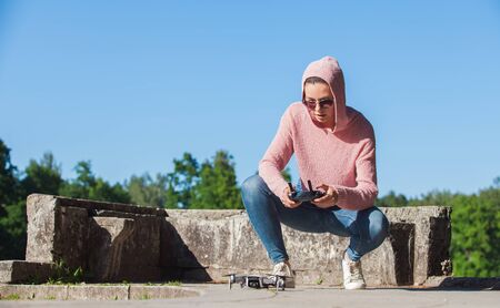 A young woman in a pink hoodie and sunglasses controlled with the remote control drone landing in...