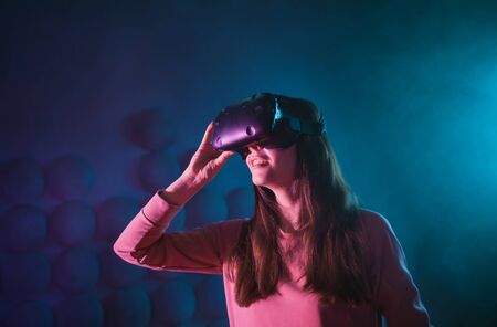 A young woman uses glasses, a virtual reality helmet on a background of a dark background in smoke....