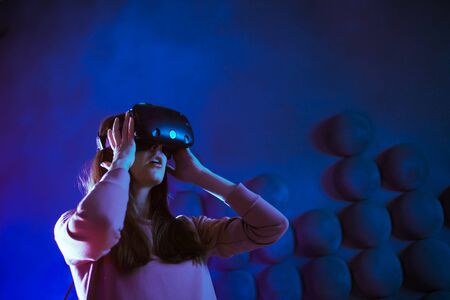 Ready for the game. The young woman in anticipation puts on virtual reality glasses, gets ready for the game, touches the air against a dark futuristic background. Copyspace.の写真素材