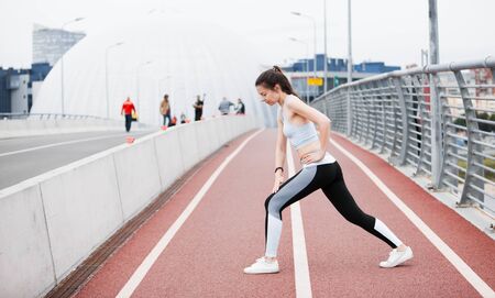 A young sports woman in a fitness suit crouches, lunges, plays sports against the backdrop of an...