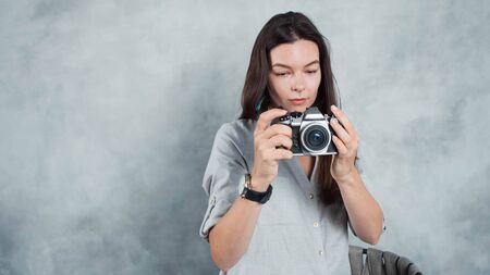 photographer takes the photo. Young successful woman contributor for photo banks. Girl with a modern camera in hand, the photographer on a gray backgroundの写真素材