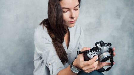photographer takes the photo. Young successful woman photo blogger. Girl with a modern camera in hand, the photographer on a gray backgroundの写真素材