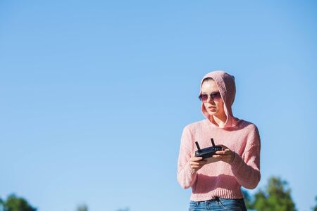 Young woman wearing sunglasses and hoodie holding a remote control, controls, controls are not...
