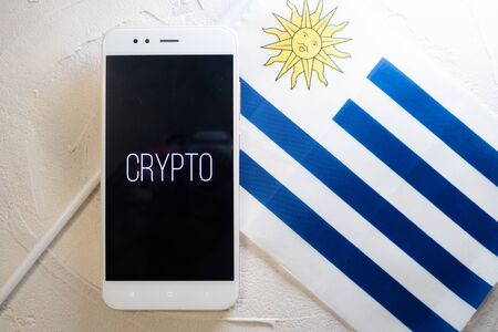 Cryptocurrency and government regulation, concept. Modern economy, smartphone with bitcoin sign on the screen on the background of the flag of Uruguayの写真素材