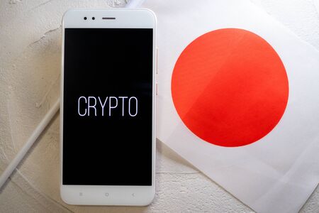 Cryptocurrency and government regulation, concept. Modern economy, smartphone with bitcoin sign on the screen on the background of the flag of Japanの写真素材