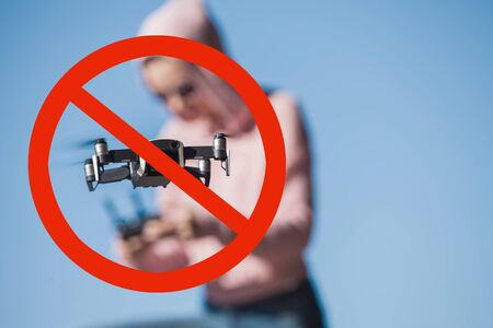 Drones are prohibited, no-fly zone. Four-propeller drone flying in nature against the blue sky and operator. The maneuver. Enclosed in red prohibition sign. Crossed out circle.の写真素材
