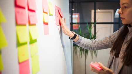 project management, agile methodology. young business woman in the office are working on a startup. Project manager plan work and stages of development of company, glue sticky leaves on Boardの写真素材