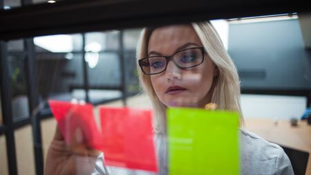 young woman in the office glues sticky sheets on the glass partition of the office. young...