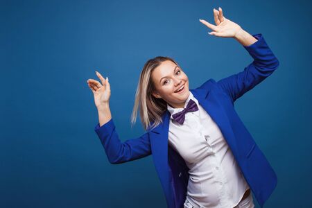 jumping and dancing businesswoman in stylish blue jacket and bow tie. Portrait of a cheerful girl on a blue background, copy spaceの写真素材