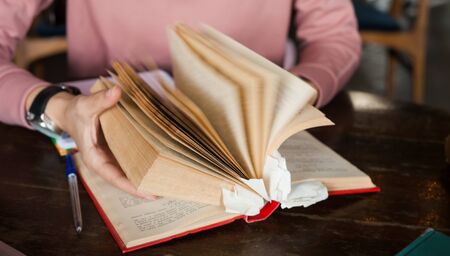 Female hands with neat manicure and a large clock leaf through a thick book with many bookmarks lying on the table. Close-up.の写真素材