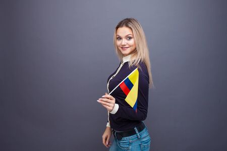 Immigration and the study of foreign languages, concept. A young smiling woman with a Colombia flag in her hand. Girl waving a Colombia flag on a gray backgroundの写真素材