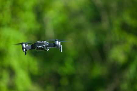 Four-propeller drone flying in nature against the green nature. The maneuver. Blurred background....