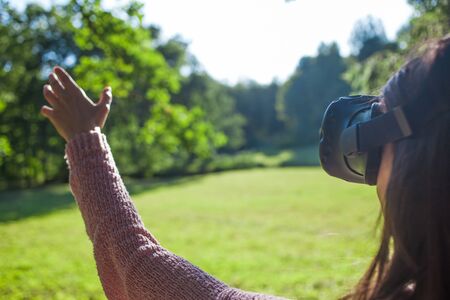 Virtual summer. A young woman in virtual reality glasses stands under the trees in a clearing, on a...