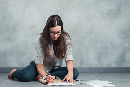 The interior designer plans the future interior sitting on the floor in an empty apartment. A young...
