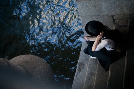 young woman in a hat and with a backpack walks in the city and uses a smartphone. Hipster on a walk uses the phone and takes photos for social networksの写真素材