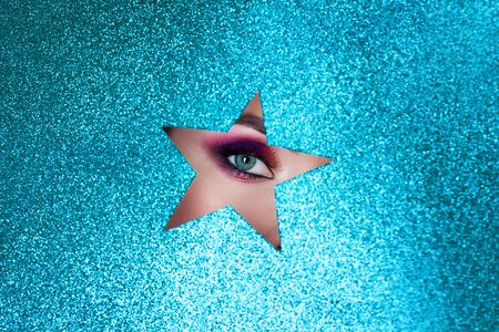 You are a superstar, bright evening makeup, a fragment of a beautiful young woman's face in a cutout in the shape of a star. Shining blue backgroundの写真素材