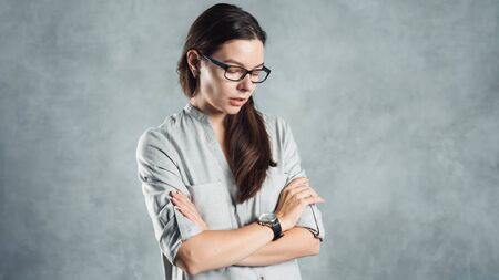 Young successful confident woman in a gray shirt against a textured gray wall. Portrait brunette in glasses, copy space on the right.の写真素材