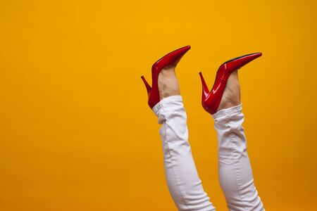 Female feet in beautiful red stiletto shoes, yellow background copy space. Women's fashion, clothing and shoesの写真素材
