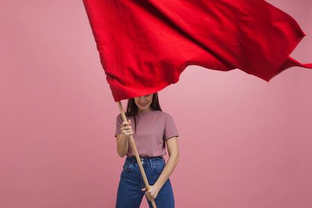 Young and beautiful girl with a red flag on a pink background. A socially active woman, to protest and fight for rights ,the conceptの写真素材